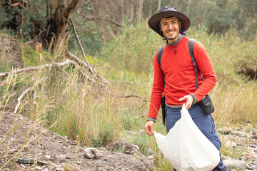mountaineer with hat picking up garbage in nature.