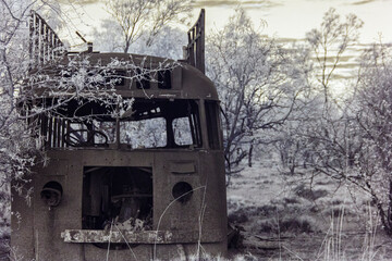 Front view of an abandoned, rusted tour bus in a forest, capture in infrared