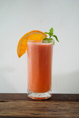 Fresh orange juice in a clear glass decorated with orange slices and mint leaves on top of the glass.On a wooden table with a white background.Include oranges, pineapple, strawberries, coconut milk.
