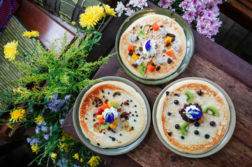 Shot from above, blueberry pancakes, mixed berry sauce, banana pancakes, chocolate chip pancakes, bananas with muesli. Pouring wild honey, in a ceramic dish on a wooden table decorated yellow flowers.