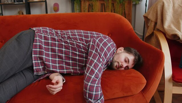 Exhausted young man in plaid shirt flopped down on sofa falls asleep. Concept of after party, tired overworked person hard day, lack of energy, breakdown. Caucasian drunk bored guy sleeping on couch.