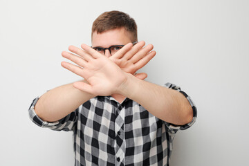 Man in checkered shirt showing stop gesture with hand, standing against a plain grey background.