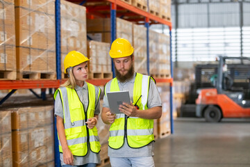Male and Female professional worker wearing safety uniform using tablet inspect goods on shelves in warehouse. supervisor worker checklist stock inspecting product in storage for logistic.