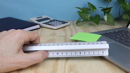 Hand holding ruler on desk background with props and green climbing plant. series of photos.