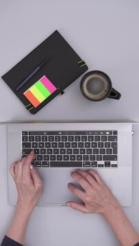 Top Shot View of a Desk With a Laptop, Notebook and Cup of Coffe on it Showing Hands Typing on a Keyboard, Vertical Video