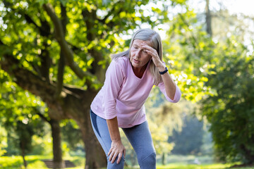 An active senior woman taking a break from running, appears tired, wiping sweat from her forehead...