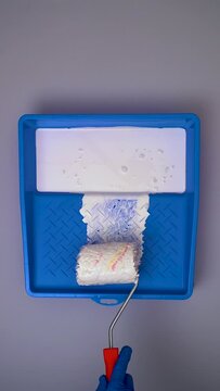 Paint Roller With White Paint Into a Blue Paint Tray on Protected Background, Vertical Video