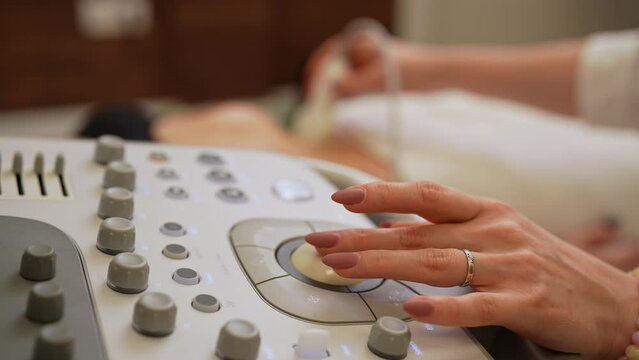 Closeup hands of female doctor using medical ultrasound machine for conducting ultrasound examination of internal organs. Professional medic performs abdominal organs sonography check up to patient.