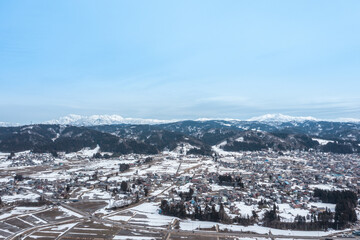 Obraz premium ドローン写真：晴れた日の冬の田舎町と雪山