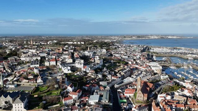 St Peter Port Guernsey colourful aerial reveal of town over harbour looking north and pulling back south to reveal buildings homes gardens and perspective of town on bright sunny day