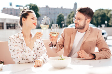 Smiling beautiful woman and her handsome boyfriend. Happy cheerful family. Couple cheering with glasses of white wine at their date in restaurant. They drinking alcohol at veranda cafe in the street