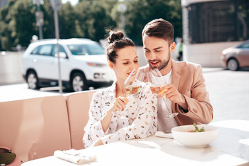 Smiling beautiful woman and her handsome boyfriend. Happy cheerful family. Couple cheering with glasses of white wine at their date in restaurant. They drinking alcohol at veranda cafe in the street
