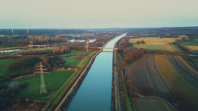 Winter sunset aerial drone view landscape navigable canal with bridges, agricultural fields and forests and farmers houses in Germany countryside. High quality 4k footage