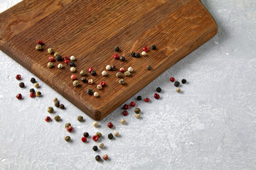 Wooden beige cutting board with scattered multicolored peppercorn peas on a gray stone countertop