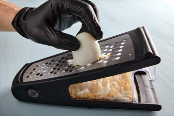 Hands in black latex gloves rub a hard-boiled chicken egg on a metal grater on a wooden countertop