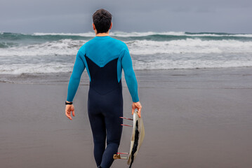 Surfer walking towards the waves on overcast day, copy space.
