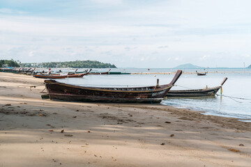 A cluster of watercraft including boats made of wood are resting on the beach, close to the water under the vast sky adorned with clouds, creating a picturesque scene at the fluid horizon.