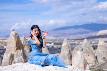 Beautiful woman in blue dress on rocks mountain. Cheerful woman relax outdoor with beautiful sky and pink flowers in holiday vacation. Woman tourist enjoy amazing mountain view. Travel and freedom..