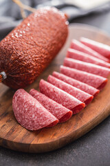Sliced smoked salami sausages on cutting board on black table.