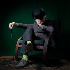 A stylish gentleman in a bowler hat and a cane sits on an armchair.