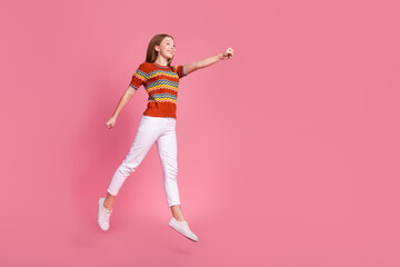 Full length portrait of overjoyed energetic girl jump raise arm fist look fly empty space isolated on pink color background