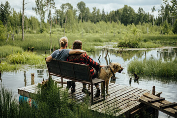 couple with dog sitting on bench in front of stomp lake surrounded by wild forest