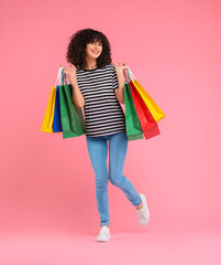 Happy young woman with shopping bags on pink background