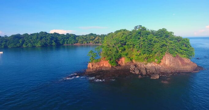 Sliding past a tree-covered outcropping to reveal two monohull sailboats in a calm bay in the Parida Islands in Panama