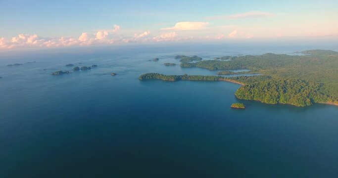 Panning aerial view high above the green jungle-covered Parida Island at golden hour in paradise