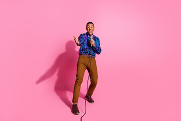 Full length photo of funky cheerful guy wear striped shirt inviting you singing microphone isolated...