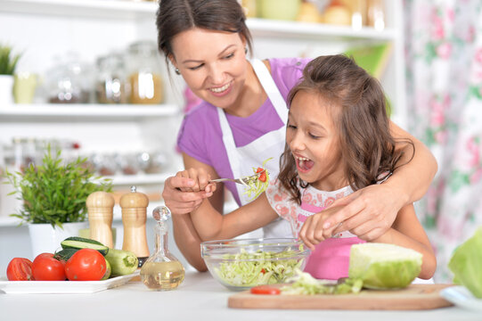 Girl with her mother cooking salad together at kitchen