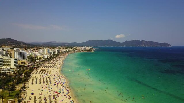 Cala major beach with turquoise waters and crowded sandy shore, sunny day, aerial view