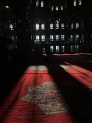 Red embroidered carpet in mosque with sun rays coming through the window, muslim religion
