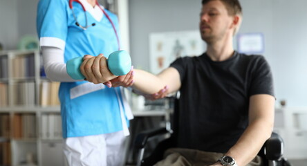 Close-up of professional medical worker helping patient work out arm. Male sitting in wheelchair. Doctor physician in uniform. Modern medicine and disabled people concept