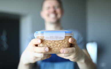 Close-up of smiling happy male worker holding plastic container with food. Macro shot of lunch. Break from work and snack. Handyman service and renovation concept