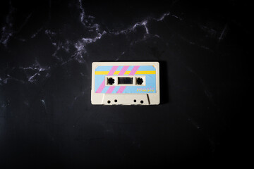 Top view a music cassette with colorful retro label on black background.