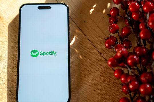 On the table is a smartphone iPhone 14 Pro Max, Spotify music streaming application logo on the screen. Casual personal background. Budapest, Hungary. November 2023.