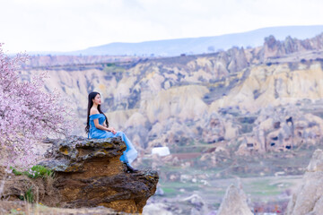 Beautiful woman in blue dress on rocks mountain. Cheerful woman relax outdoor with beautiful sky and pink flowers in holiday vacation. Woman tourist enjoy amazing mountain view. Travel and freedom..