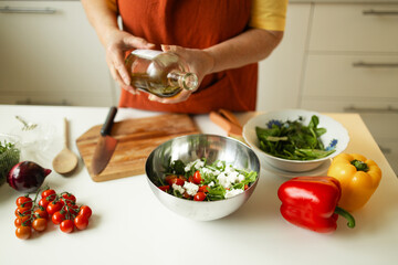 Woman seasons a vegetable salad while preparing food in the kitchen. Unrecognizable chef adds olive oil while preparing a vegetarian meal at home. Healthy eating concept. 