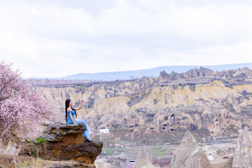 Beautiful woman in blue dress on Turkey rocks mountain.Cheerful woman relax outdoor with beautiful sky and pink flowers in holiday vacation.Woman tourist enjoy amazing mountain view.Travel and freedom