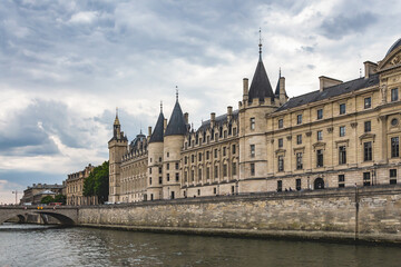 Fototapeta na wymiar Conciergerie palace and prison on the Ile de la Cite. View from Seine river. Cloudy sky at background. Paris, France