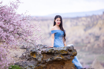 Beautiful woman in blue dress on rocks mountain. Cheerful woman relax outdoor with beautiful sky and pink flowers in holiday vacation. Woman tourist enjoy amazing mountain view. Travel and freedom..