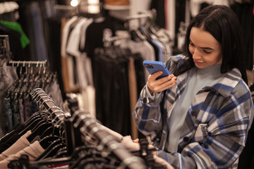 Beautiful brunette girl scanning barcode with her smartphone in clothes store