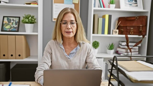 Blonde woman working at laptop in a modern office interior with plants and books