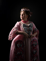 close upProfile portrait of female model wearing an opulent pink gown, costume of a historical French baroque nobility, style of Marie Antoinette. Isolated dark cinematic silhouette studio background