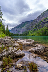 A scene of a lake in a deep mountain valley with rocks submerged in the foreground, Avalanche Lake,...