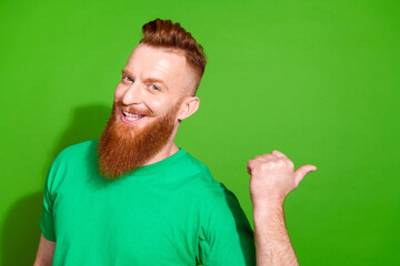 Photo of optimistic man with ginger beard dressed stylish t-shirt indicating at proposition empty space isolated on green color background