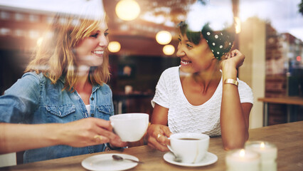 Two multi ethnic friends enjoying coffee in a cafe window - 748024505