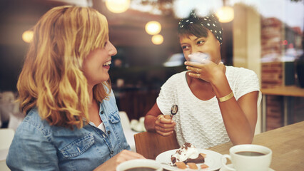 Two diverse smiling friends enjoying a cup of coffee and cake in a cafe