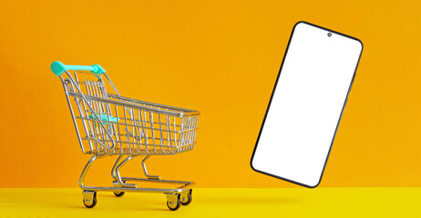 Shopping cart with smartphone and orange background with copy space for put your text or logo. Shopping Online on Website or Mobile Application
